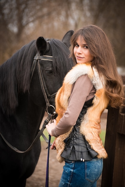 Girl with a horse on ranch onn autumn cloudy day.