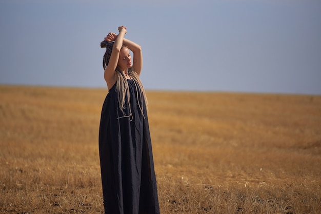 A girl with long dreadlocks romantically stands in the field raising her hands up high quality photo