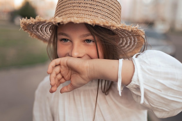 Girl with long hair and freckles in a straw hat laughs and covers her hand