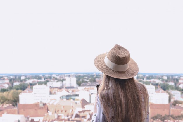 A girl with long hair in a hat stands on the observation deck and looks at the city of Graz.