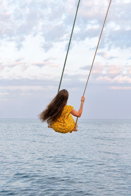 Photo girl with long hair is riding swing above the water. vertical frame.