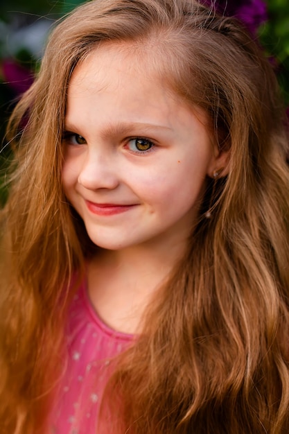 A girl with long hair and a pink shirt smiles.