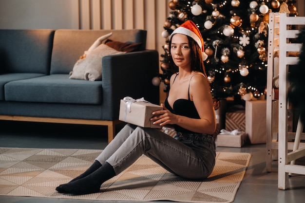 A girl with a new year's gift in her hands is sitting at home near the Christmas tree