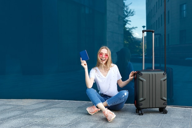 Girl with passport and luggage in pink glasses on a blue background