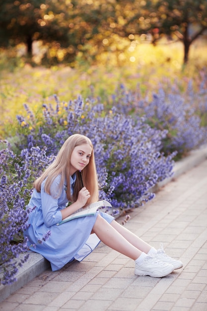 Girl with pen writes in a notebook, sitting in the Park in the flowers outside