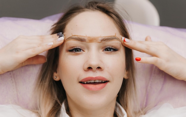 Girl with permanent makeup on her eyebrows The makeup artist makes markings with a brown pencil for eyebrow tattooing