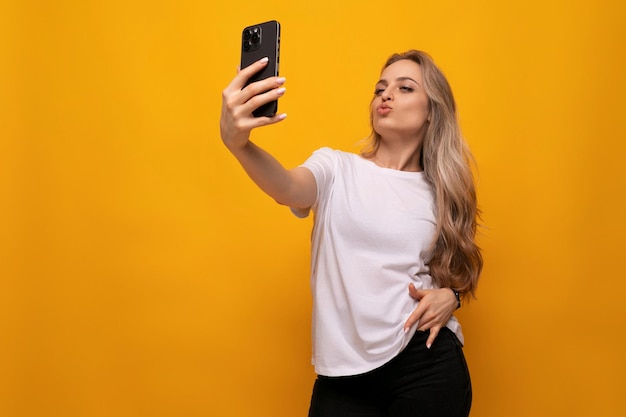 A girl with a phone in her hands admires herself on a yellow background