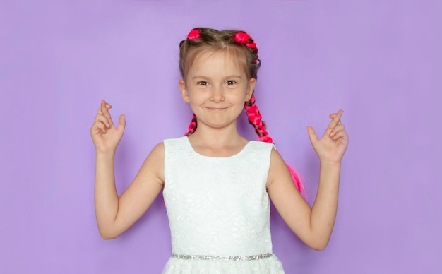 A girl with pink hair crossed her fingers makes a wish waits for good news on a purple background Crosses his fingers for luck while waiting for the results of the lottery or exams