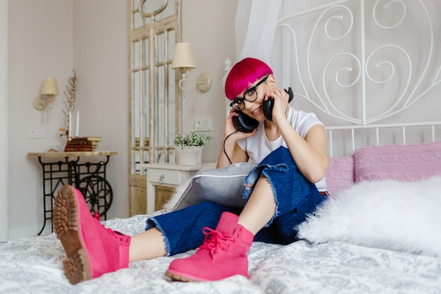 Girl with pink hair listens to music and rests on the bed