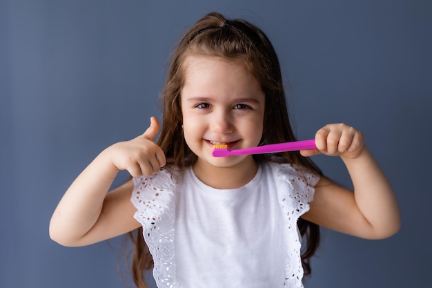 A girl with a pink toothbrush and a thumbs up sign