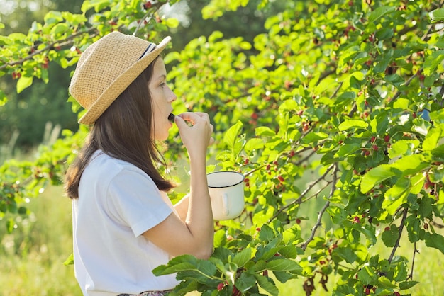 Girl with pleasure eating delicious sweet ripe berries from mulberry tree. Summer season in garden, natural organic berries, rich in vitamins, healthy food