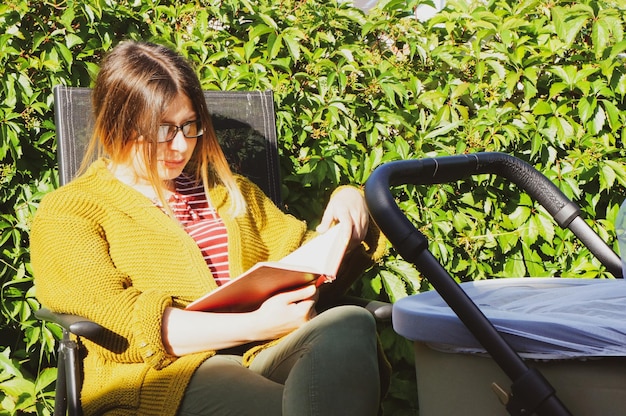 A girl with a pram reads a book in nature on a summer sunny day