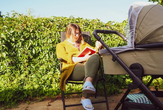 A girl with a pram reads a book in nature on a summer sunny day