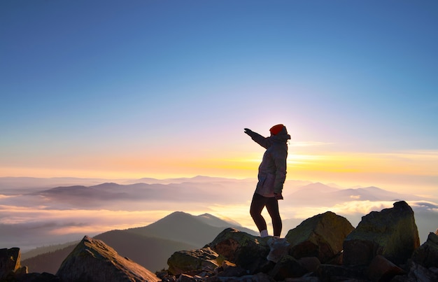 Girl with raised hand on the mountain peak at beautiful morning sunrise.