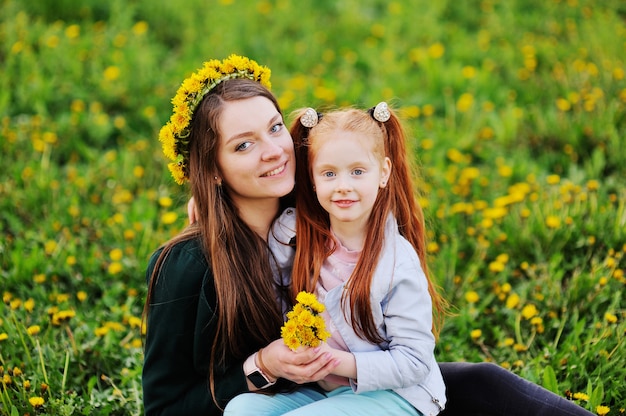 Photo girl with red hair hugs her mom on the background of a field with dandelions