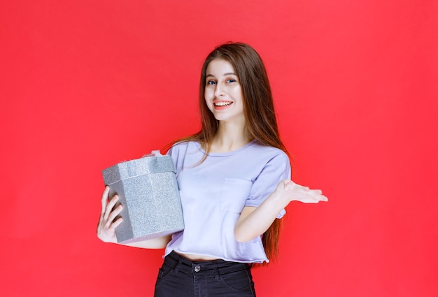 Girl with a silver gift box noticing and inviting the person ahead to receive it. 