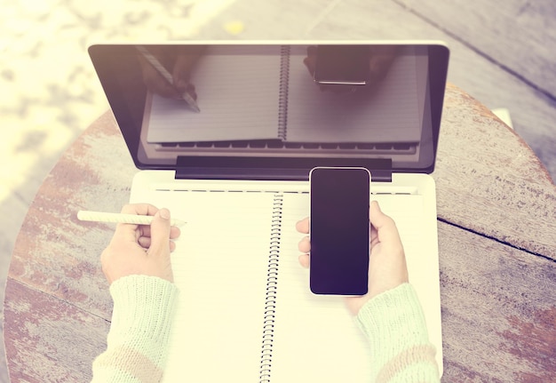 Girl with smartphone blank diary with pen and laptop on a wooden table