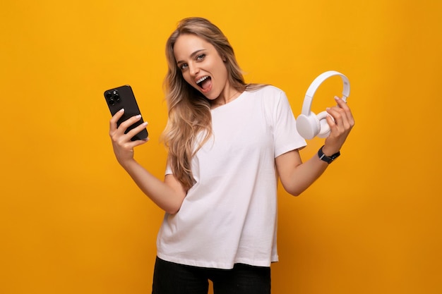 A girl with a smartphone and headphones in her hands uses an application on an orange background