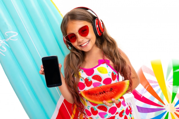 girl with summer glasses, headphones, a cocktail and a phone on the wall of inflatable swimming mattresses