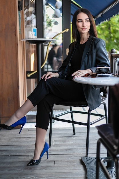 Girl with sunglasses sitting in a cafe, coffee shop, sitting on a chair in the city with red flowers, wearing sun glasses