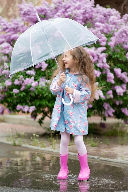 A girl with a transparent umbrella against the background of blooming lilacs enjoys spring