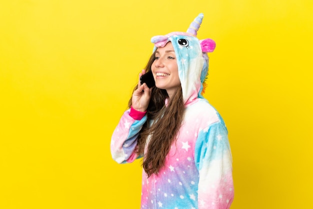 Girl with unicorn pajamas over isolated background keeping a conversation with the mobile phone