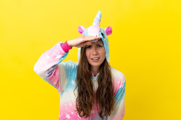 Girl with unicorn pajamas over isolated background looking far away with hand to look something