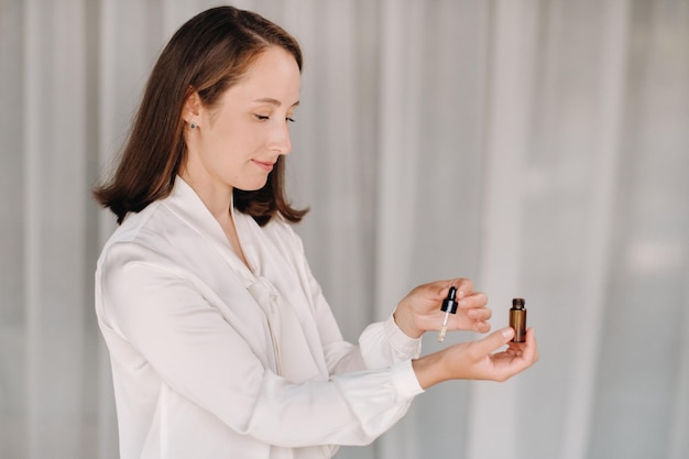 A girl with a white blouse holds essential oils in her hands and drips on her wrist