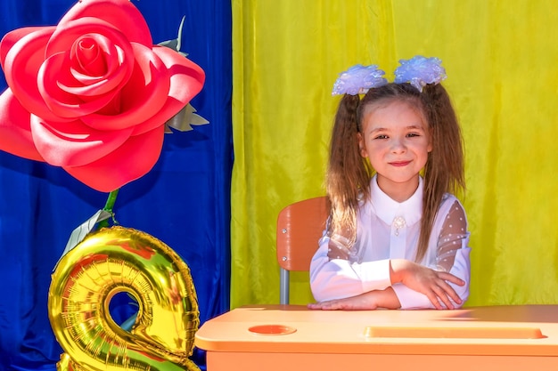 A girl with white bows and a white blouse smiles during the celebration of the first of September.