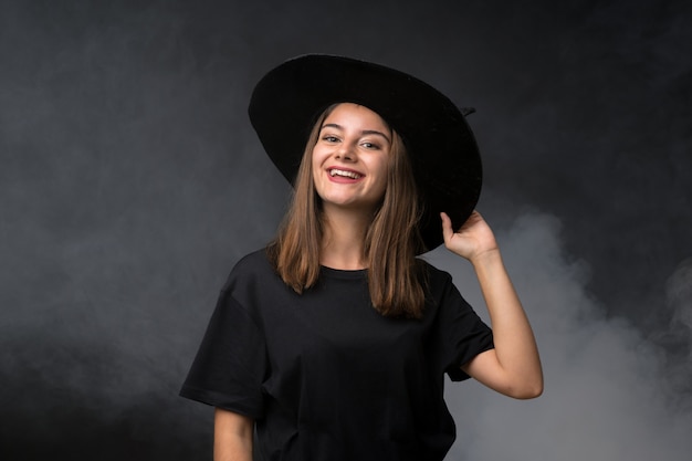 Girl with witch costume for halloween parties over isolated dark wall laughing