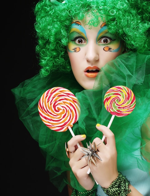 Girl with with creative make-up holds lollipop