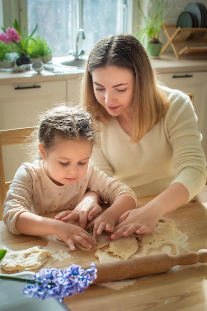 Girl and woman cook at home in a kitchen a child stirs flour knead the dough on the table by hand