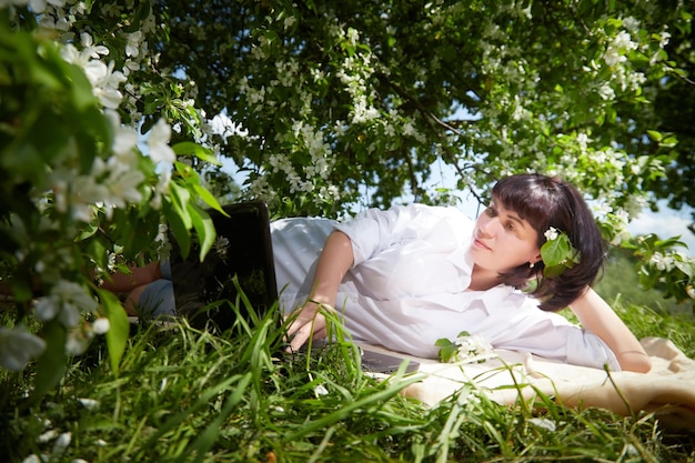 Photo girl working on laptop in blossoming garden middle aged woman using computer in white apple blossoms