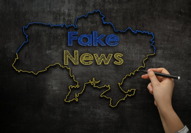 The girl writes on the blackboard the text fake news in the map of ukraine