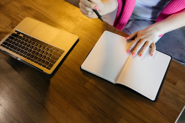 The girl writes in a notebook The girl sits and writes in a notebook Laptop near female hands Young girl doing Notebook and notebook on a wooden table Business education freelance concept