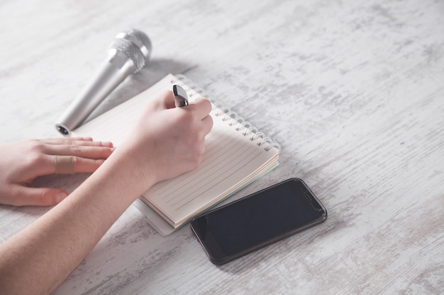 Girl writing on notepad. Microphone and smartphone on the desk