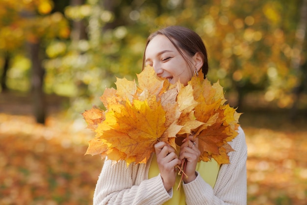 Girl in yellow clothes in autumn park rejoices in autumn holding yellow leaves in her hands warm