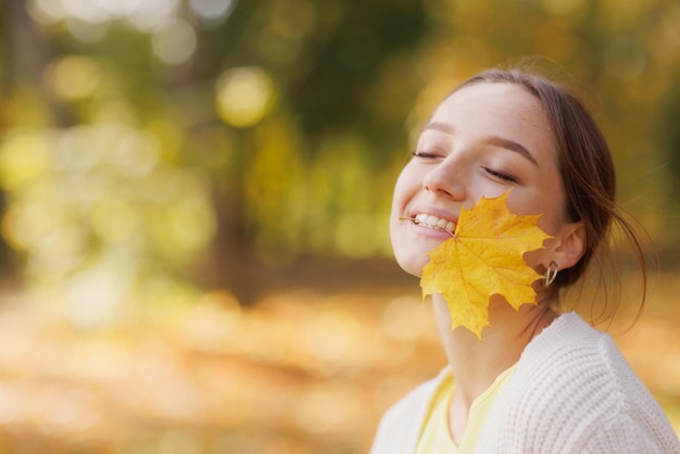 Girl in yellow clothes in autumn park rejoices in autumn holding yellow leaves in her hands warm