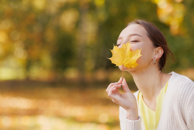 Girl in yellow clothes in autumn park rejoices in autumn holding yellow leaves in her hands warm