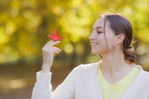 Girl in yellow clothes in autumn park rejoices in autumn holding yellow leaves in her hands warm