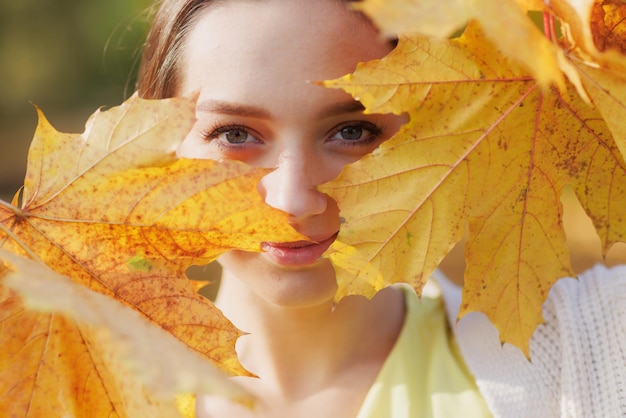 a girl in yellow clothes in an autumn park rejoices in autumn holding yellow leaves in her hands