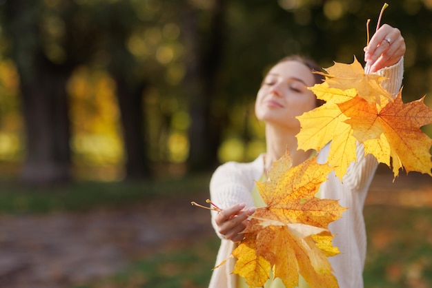 a girl in yellow clothes in an autumn park rejoices in autumn holding yellow leaves in her hands