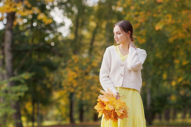 a girl in yellow clothes in an autumn park rejoices in autumn holding yellow leaves in her hands