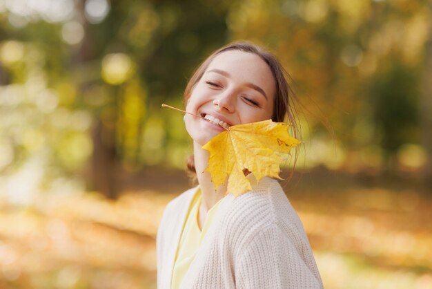 a girl in yellow clothes in an autumn park rejoices in autumn holding yellow leaves in her hands