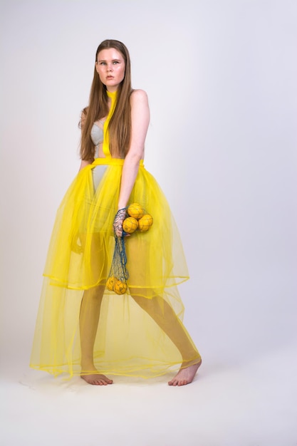 A girl in a yellow dress with a bag of lemons on a white background