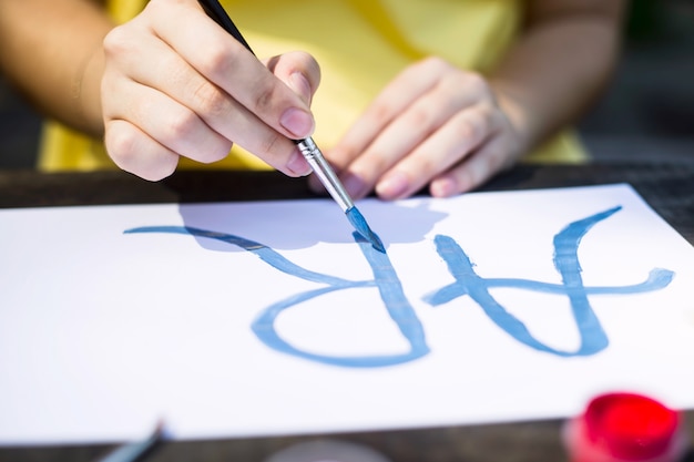 A girl in a yellow dress writes paints on a sheet of paper the word art. 