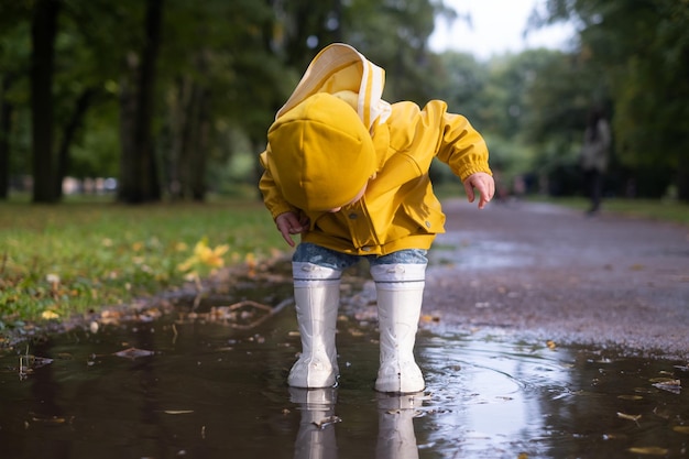 Girl in yellow jacket and white rubber boots is running over a puddle