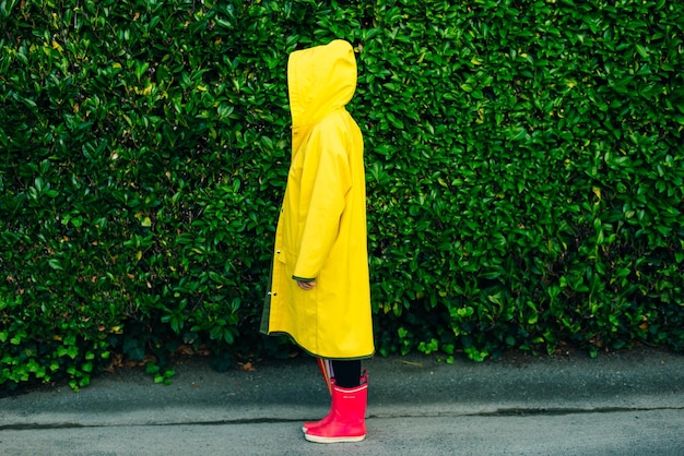 Girl in a yellow raincoat on a background of a wall with grass