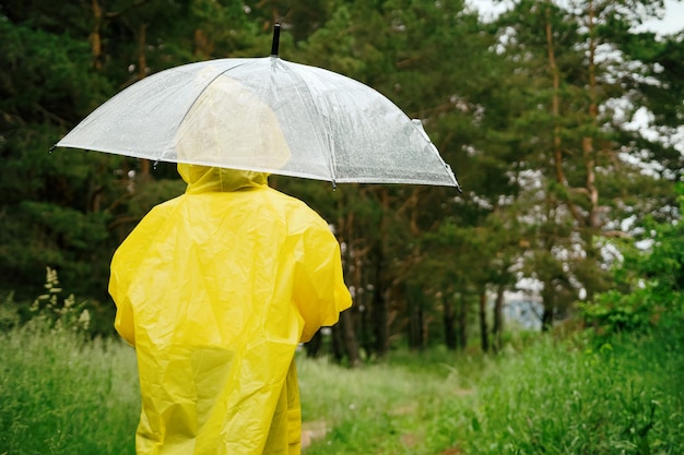 Girl in yellow raincoat hides under umbrella from rain