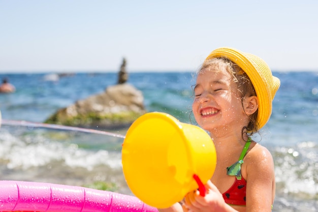 Girl in yellow straw hat plays with the wind water and a water dispenser in an inflatable pool on the beach Indelible products to protect children's skin from the sun sunburn resort at the sea